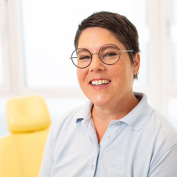 Porträt von Alexandra Präger vor einem unscharfen Hintergrund. Sie trägt ein hellblaues Polo-Shirt und lächelt freundlich in die Kamera