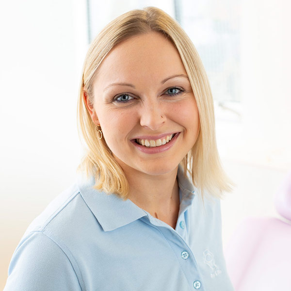 Porträt von Elisabeth Krochmann vor einem unscharfen Hintergrund. Sie trägt ein hellblaues Polo-Shirt und lächelt freundlich in die Kamera