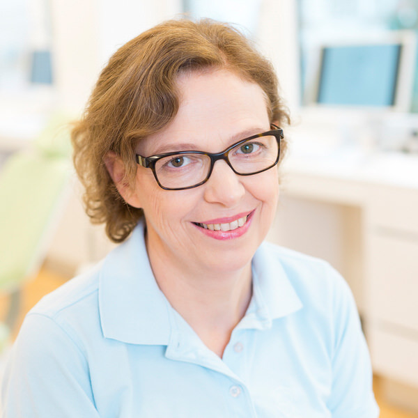 Porträt von Elisabeth Müller vor einem unscharfen Hintergrund. Sie trägt ein hellblaues Polo-Shirt und lächelt freundlich in die Kamera