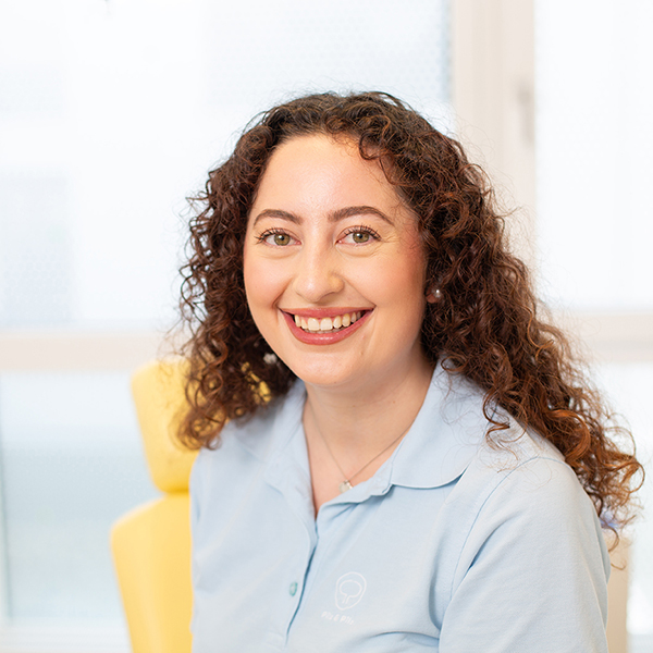 Porträt von Melissa Eser vor einem unscharfen Hintergrund. Sie trägt ein hellblaues Polo-Shirt und lächelt freundlich in die Kamera