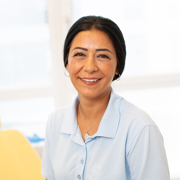 Porträt von Rukiye Karabacak vor einem unscharfen Hintergrund. Sie trägt ein hellblaues Polo-Shirt und lächelt freundlich in die Kamera